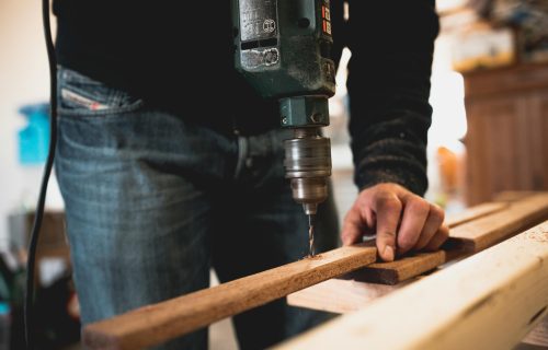 Close-up of a person using an electric drill on a wooden plank, showcasing detailed woodworking skills.