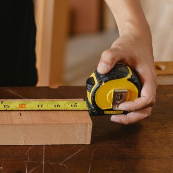 Close-up of carpenter's hand measuring wood with a tape measure in a workshop.