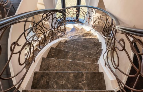 From above of spiral stairway with marble steps and metal railings with decorative elements located in modern light building with window